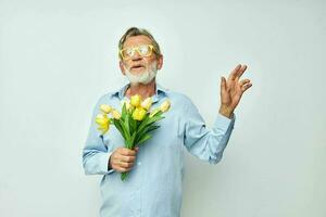 mayor canoso hombre un ramo de flores de flores con lentes como un regalo ligero antecedentes foto