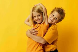 Boy and girl in yellow t-shirts standing side by side childhood emotions yellow background photo