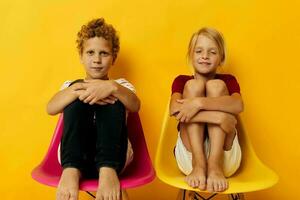 Small children childhood sitting on chairs together on colored background photo