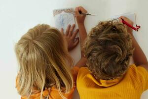 dos alegre niños dibujo en cuadernos acostado en el piso ligero antecedentes inalterado foto