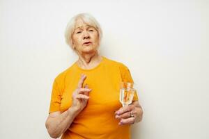 smiling elderly woman in yellow t-shirts a glass of water in his hands cropped view photo