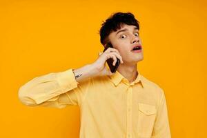 joven chico en amarillo camisa hablando en el teléfono aislado antecedentes foto