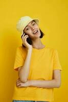 young woman yellow t-shirt and Hat summer style with phone yellow background photo