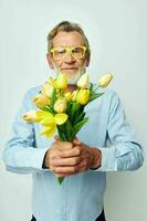 Photo of retired old man in a blue shirt with a bouquet of flowers light background