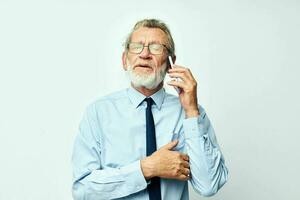 old man in glasses with a phone in the studio on a white background talking photo