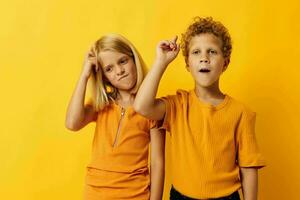 Boy and girl in yellow t-shirts standing side by side childhood emotions yellow background photo