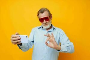 elderly man in fashionable red glasses with a phone yellow background photo