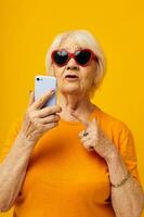 smiling elderly woman in casual t-shirt communication by phone yellow background photo