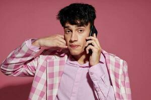 A young man fashionable talking on the phone pink blazer posing studio pink background unaltered photo