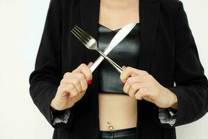 photo pretty woman in a black jacket a knife and a fork near the face light background