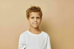 Cheerful boy with curly hair in a white t-shirt beige background photo