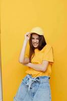 optimista joven mujer posando en un amarillo camiseta y gorra amarillo antecedentes foto