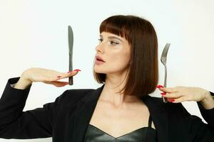 foto bonito mujer en un negro chaqueta un cuchillo y un tenedor cerca el cara ligero antecedentes