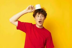 Young curly-haired man posing with a white mug and in the hands of a drink yellow background unaltered photo