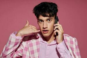 A young man fashionable talking on the phone pink blazer posing studio pink background unaltered photo