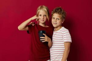 boy and girl are standing next to a disposable glass with a drink red background photo