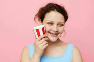 alegre niña con un desechable multicolor vaso en un rosado antecedentes foto