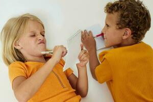 imagen de positivo chico y niña dibujo en cuadernos acostado en el piso ligero antecedentes inalterado foto