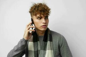 hermoso joven hombre en un tartán bufanda mirando a el teléfono Moda ligero antecedentes foto