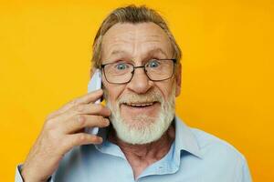 Photo of retired old man gray beard with glasses talking on the phone yellow background