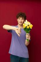 un joven hombre participación un amarillo ramo de flores de flores púrpura camisetas rojo antecedentes inalterado foto