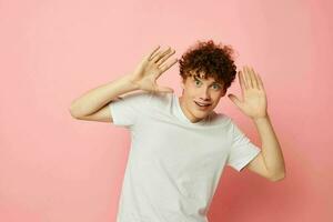 Young curly-haired man posing youth style white t-shirt pink background unaltered photo