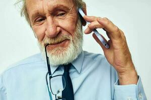 Photo of retired old man in a shirt with a tie with a phone technology light background