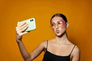 joven hermosa mujer brillante maquillaje posando negro jersey con un teléfono en mano amarillo antecedentes inalterado foto