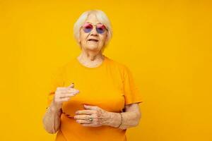 smiling elderly woman in a yellow t-shirt posing yellow background photo