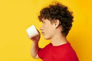 cute red-haired guy posing with a white mug and in the hands of a drink yellow background unaltered photo