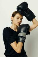 young woman in boxing gloves in black pants and a T-shirt light background photo