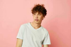 Young curly-haired man posing youth style white t-shirt pink background unaltered photo