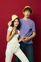 young man and girl in colorful t-shirts stylish clothes hats red background photo