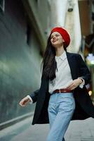 Fashion woman smile with teeth portrait walking tourist in stylish clothes in jacket with red lips walking down narrow city street flying hair, travel, cinematic color, retro vintage style. photo