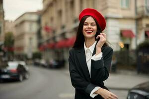 Moda mujer sonrisa con dientes en pie en el calle en frente de el ciudad turista en elegante ropa con rojo labios y rojo boina, viajar, cinematográfico color, retro Clásico estilo, urbano moda. foto