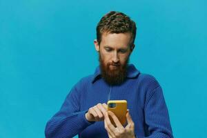 Portrait of a man with a phone in his hands does looking at it and talking on the phone, on a blue background. Communicating online social media, lifestyle photo