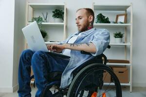 un hombre en un silla de ruedas persona de libre dedicación trabajos a un ordenador portátil a hogar, trabajo en línea, social redes y puesta en marcha, Copiar espacio, integración dentro sociedad, concepto de salud discapacitado persona, real persona de cerca foto