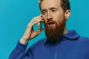 Portrait of a man with a phone in his hands does looking at it and talking on the phone, on a blue background. Communicating online social media, lifestyle photo