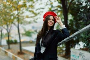 Moda mujer caminando abajo pasos en contra ciudad fondo en elegante ropa con rojo labios y rojo boina, viajar, cinematográfico color, retro Clásico estilo, urbano Moda estilo de vida. foto