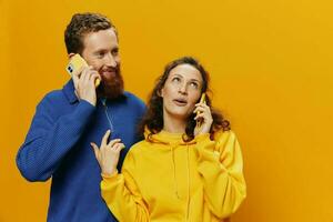 hombre y mujer Pareja sonriente alegremente con teléfono en mano social medios de comunicación visita fotos y vídeos, en amarillo fondo, símbolos señales y mano gestos, familia autónomos