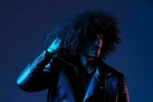 Portrait of fashion man with curly hair on blue background multinational, colored light, black leather jacket trend, modern concept. photo