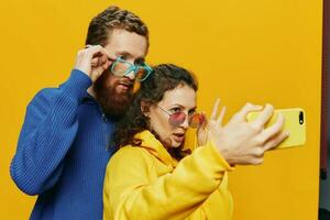 Woman and man funny couple with phones hand social networking and communication crooked do selfies smile fun, on yellow background. The concept of real family relationships, freelancers, work online. photo