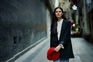 Fashion woman smile with teeth and fun tourist in stylish clothes in jacket and red beret walking down narrow city street flying hair, travel, French style, cinematic color, retro style. photo