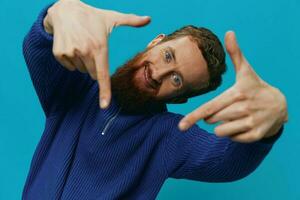 Portrait of a man in a sweater smile and happiness, hand signs and symbols, on a blue background. Lifestyle positive, copy place. photo