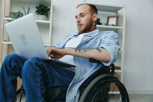 A man in a wheelchair freelancer works at a laptop at home, work online, social networks and startup, copy space, integration into society, concept of health disabled person, real person close-up photo