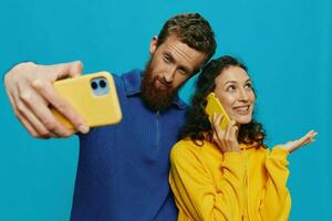 Woman and man funny couple with phones in hand taking selfies crooked smile fun, on blue background. The concept of real family relationships, talking on the phone, work online. photo