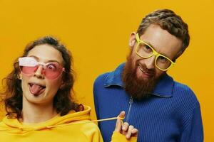 Man and woman couple smiling cheerfully and crooked with glasses, on yellow background, symbols signs and hand gestures, family shoot, newlyweds. photo