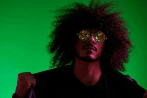 Fashion portrait of a man with curly hair on a green background with sunglasses, multinational, colored pink light, trendy, modern concept. photo