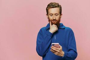 Portrait of a man with a phone in his hands doing looking at it and talking on the phone, on a pink background. Communicating online social media, lifestyle photo