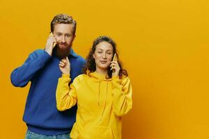 Man and woman couple smiling merrily with phone in hand social media viewing photos and videos, on yellow background, symbols signs and hand gestures, family freelancers.